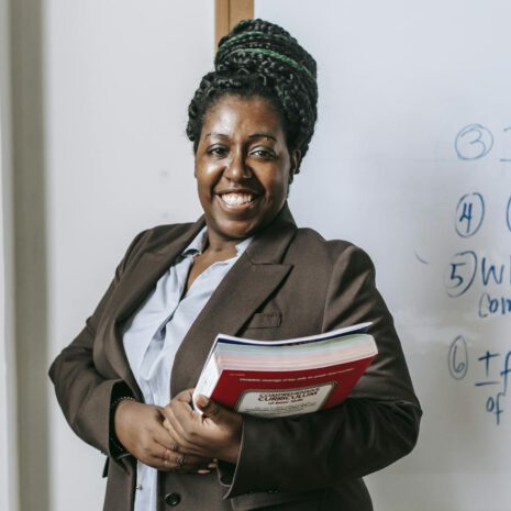Happy black female teacher  standing with workbooks near whiteboard